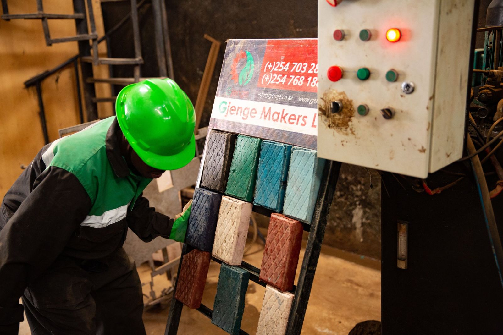 A rack of colourful Gjenge paving bricks beside the production machine