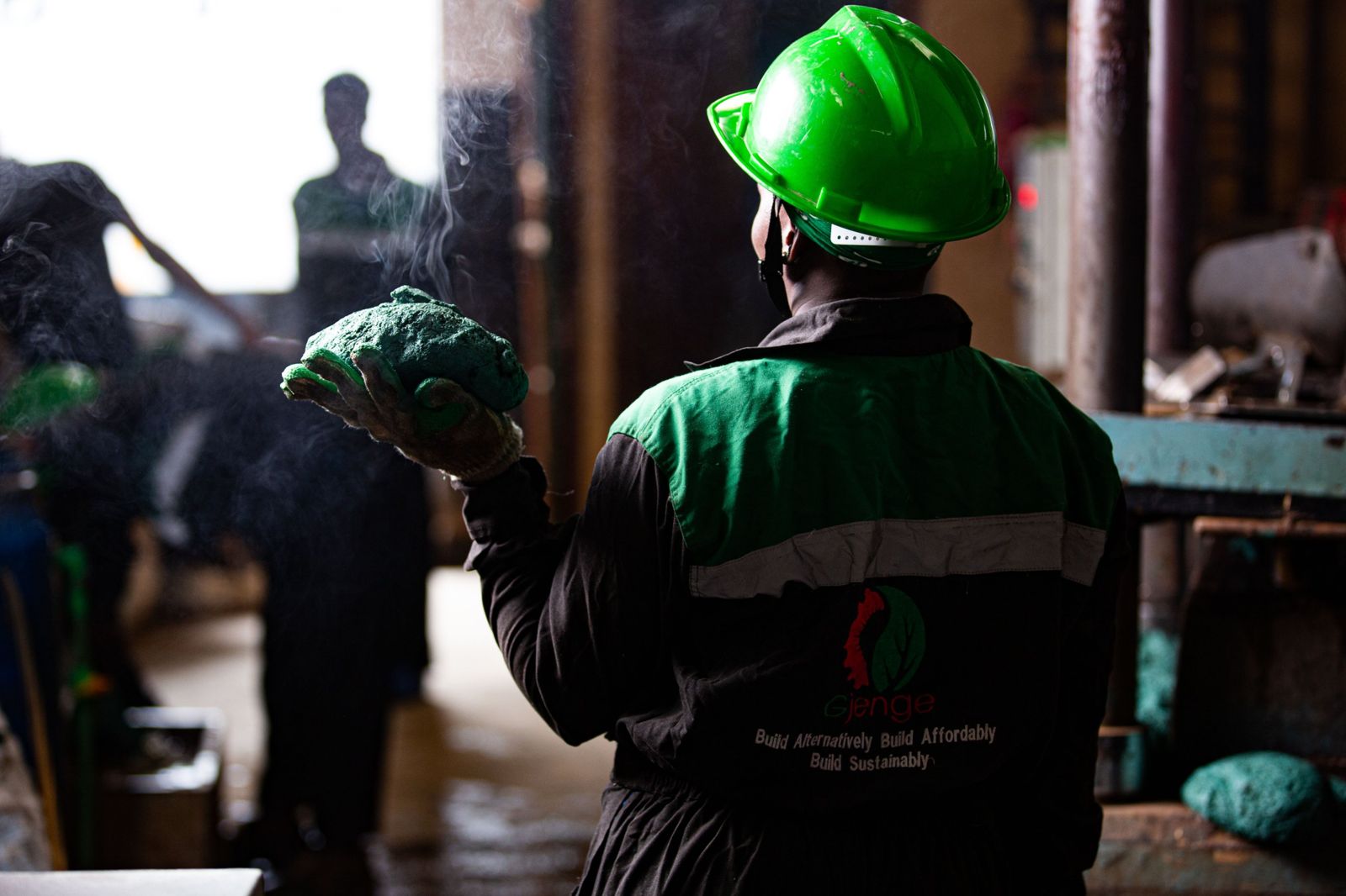 A Gjenge worker in a green hard hat holding a steaming block of green recycled plastic